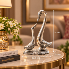Silver-toned swan figurine set on a round table in a living room setting, with overlaid dimension lines showing 14 cm height, 13.5 cm width, and 7.