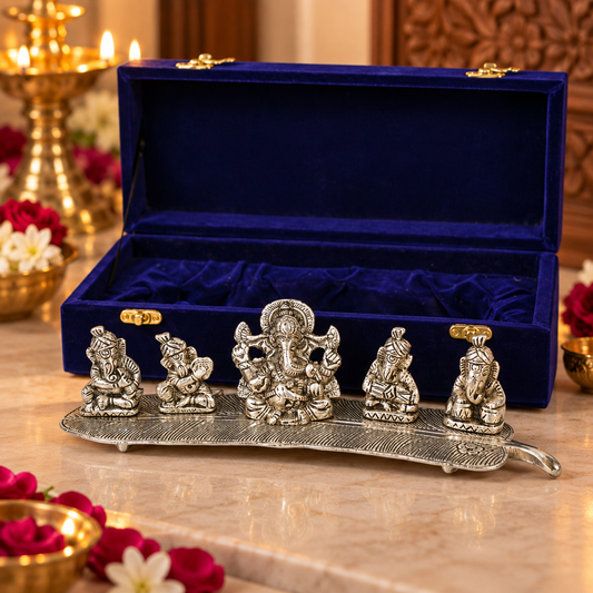 A set of five silver Ganesha figurines displayed on a decorative silver tray, with an open royal blue velvet presentation box behind them on a marble surface.