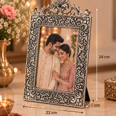 An ornate silver-toned metal picture frame with intricate scrollwork, standing on a marble surface. The frame contains a photo of a couple, with dimension lines indicating its height as 34 cm and width as 22 cm.