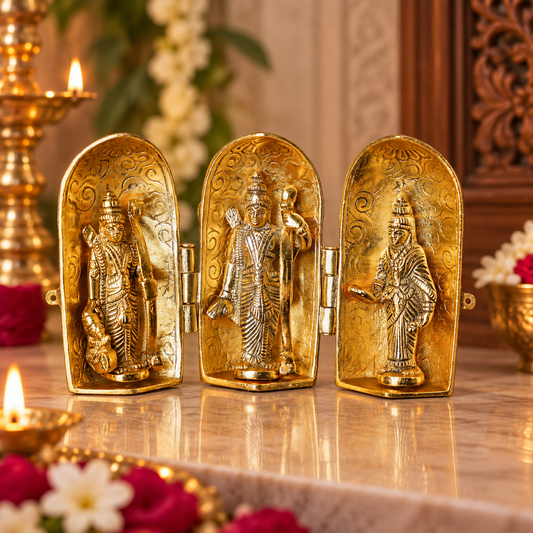Three gold-toned Hindu deity figurines displayed side by side in arched niches, set on a polished marble surface with warm decorative background elements including flowers and lit candles.
