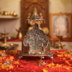 Decorative silver metal object on a red cloth with flowers, in a warm-toned room.