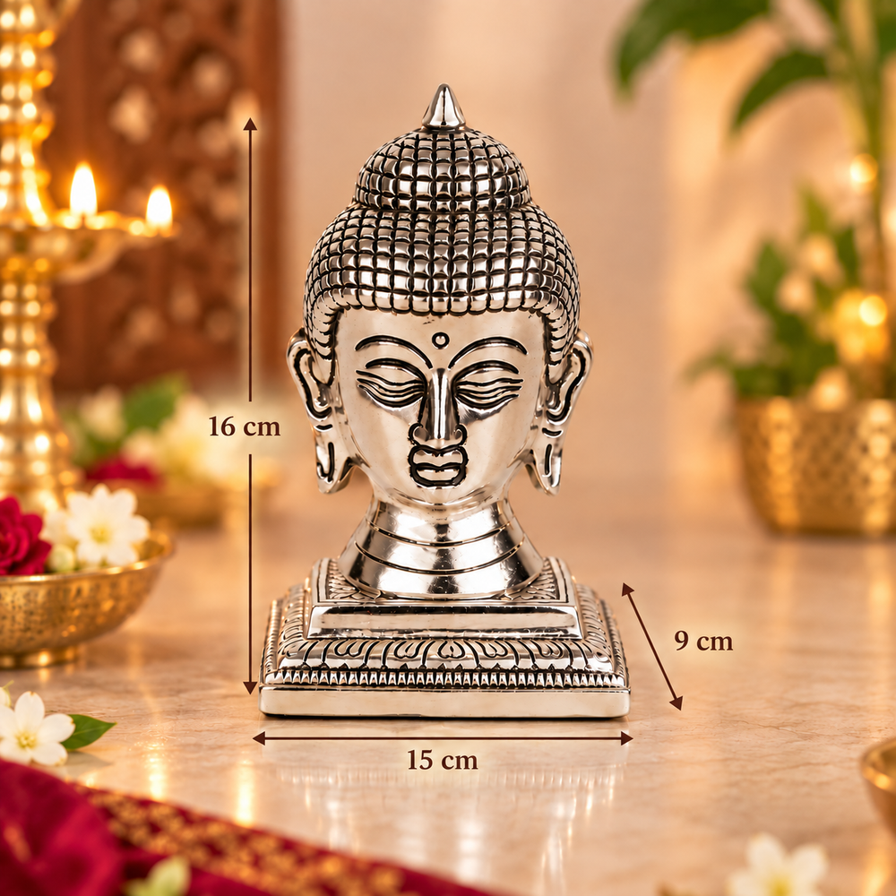 Silver-toned Buddha head statue on a decorative base, shown with dimension arrows and labels indicating 16 cm height, 9 cm width, and 15 cm depth, against a softly blurred warm indoor background.