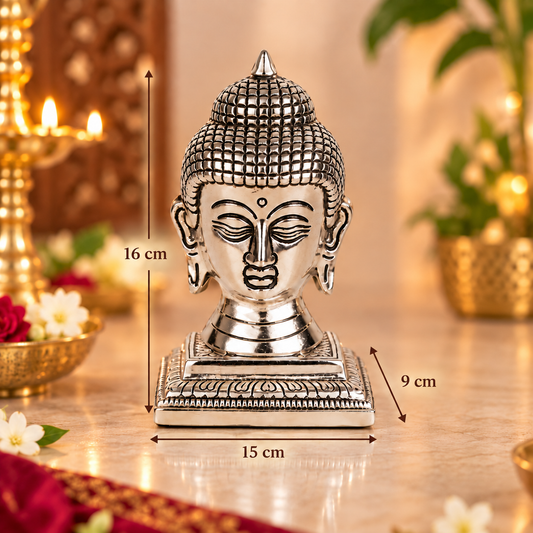Silver-toned Buddha head statue on a decorative base, shown with dimension arrows and labels indicating 16 cm height, 9 cm width, and 15 cm depth, against a softly blurred warm indoor background.