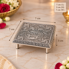 An ornate silver-toned metal stand with a carved deity Ganesha design, shown on a marble surface with dimension overlays indicating 7 cm length, 3 cm height, and 7 cm width.