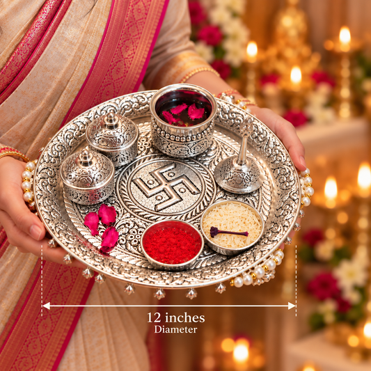 An ornate silver ritual tray held by a person wearing a beige and pink sari, with decorative bowls, flowers, and lit candles in the background. White text at the bottom reads '12 inches Diameter' with a measurement arrow.