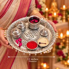 An ornate silver ritual tray held by a person wearing a beige and pink sari, with decorative bowls, flowers, and lit candles in the background. White text at the bottom reads '12 inches Diameter' with a measurement arrow.