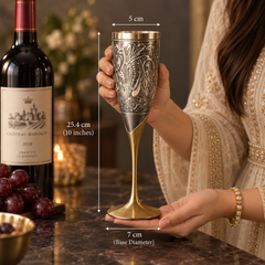 A decorative metal goblet with an ornate silver-toned floral engraving and a gold-toned stem and base, held by a woman in a cream embroidered dress. White dimension lines label the height as 25.