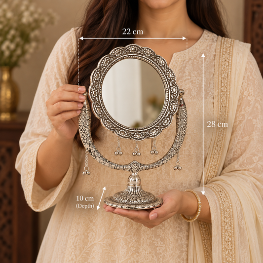 A woman in a beige embroidered traditional outfit holds a decorative silver-toned oval vanity mirror with ornate detailing and hanging tassels. White dimension lines and text show the mirror's height as 28 cm, width as 22 cm, and depth as 10 cm.