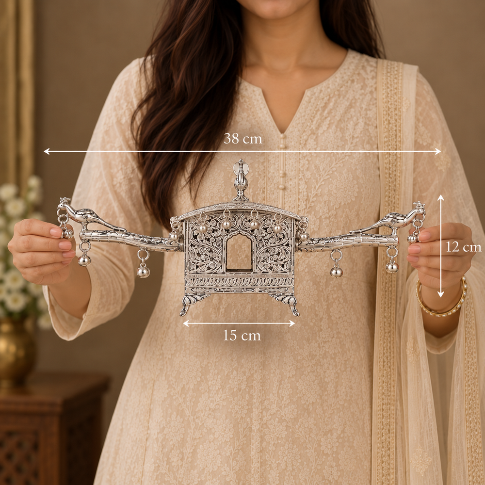 A woman in a beige embroidered kurta holds a silver-toned ornate decorative wall hanging or ornament. White dimension arrows and labels overlay the product, showing 38 cm width, 15 cm lower width, and 12 cm height.