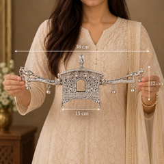 A woman in a beige embroidered kurta holds a silver-toned ornate decorative wall hanging or ornament. White dimension arrows and labels overlay the product, showing 38 cm width, 15 cm lower width, and 12 cm height.