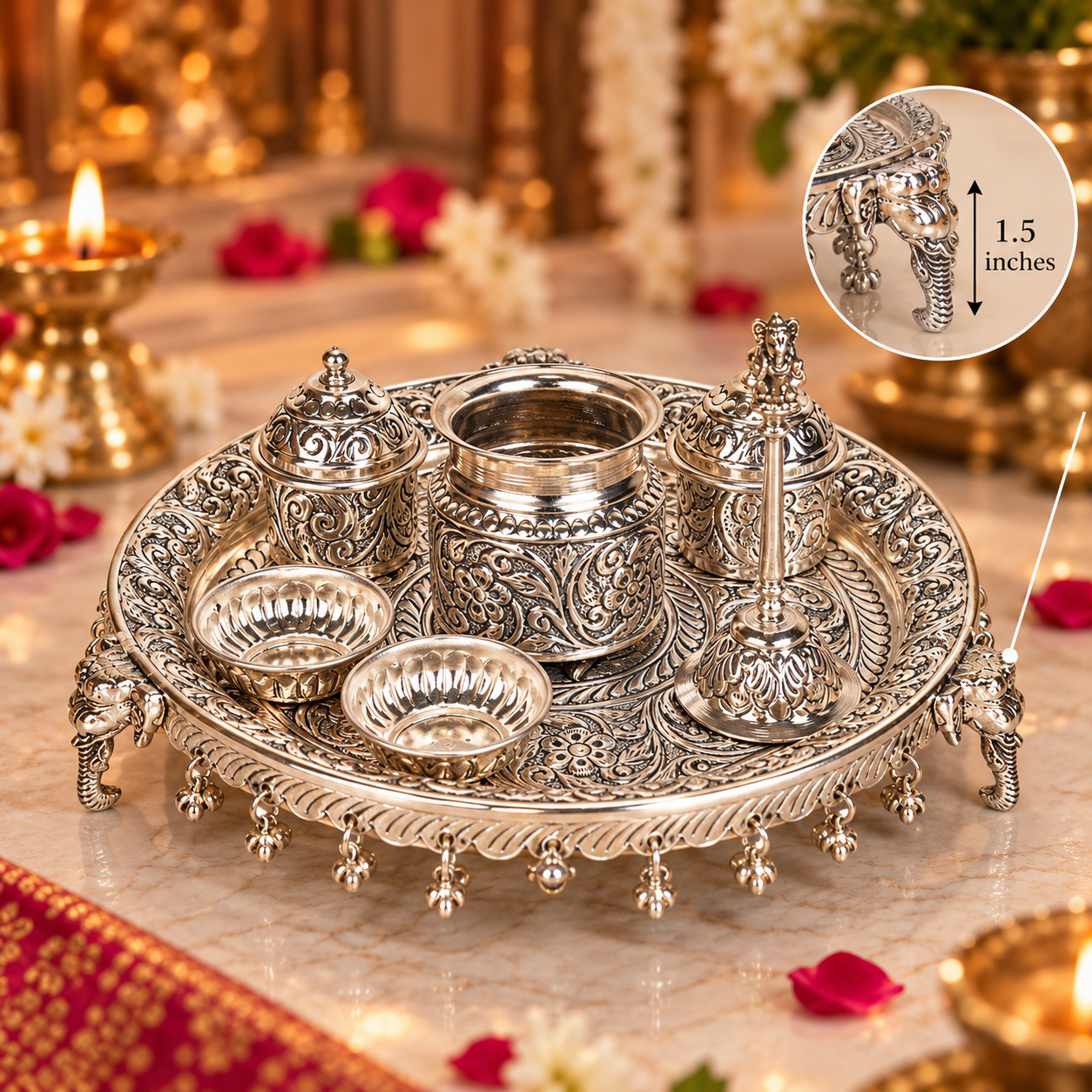 An ornate silver-toned metal tray set with carved floral detailing and elephant-shaped feet, shown on a marble surface with lit candles and flowers in a decorative setting. A circular inset at the top right shows a close-up of a small elephant-shaped detail labeled 1.