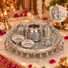 An ornate silver-toned metal tray set with carved floral detailing and elephant-shaped feet, shown on a marble surface with lit candles and flowers in a decorative setting. A circular inset at the top right shows a close-up of a small elephant-shaped detail labeled 1.