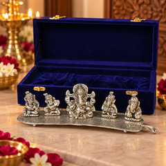 A set of five silver Ganesha figurines displayed on a decorative silver tray, with an open royal blue velvet presentation box behind them on a marble surface.