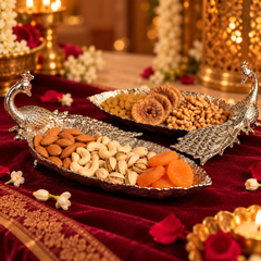 Decorative silver peacock-shaped trays filled with almonds, cashews, pistachios, dried figs, and apricots, arranged on a deep red velvet cloth with flowers and warm ambient lighting.
