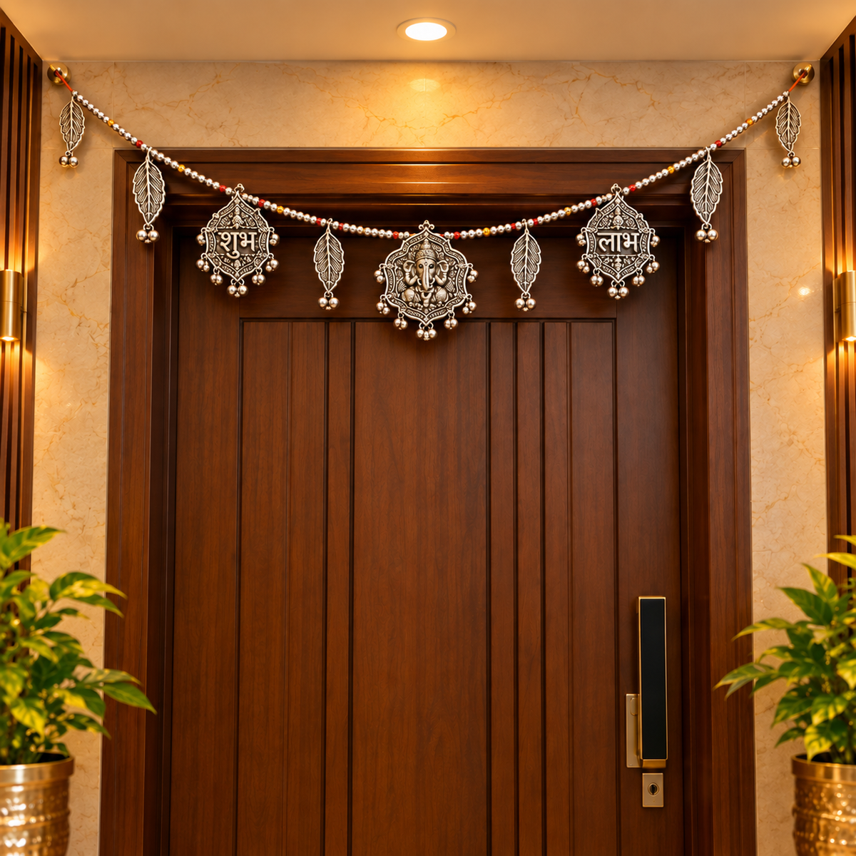 An ornate silver Ganesha door hanging decorated with intricate metal ornaments and hanging text, displayed on a dark wooden door in a warm, decorated home interior.