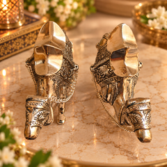 A pair of ornate metallic elephant figurines with intricate engraved details and chain accents, displayed on a marble surface with warm decorative lighting.