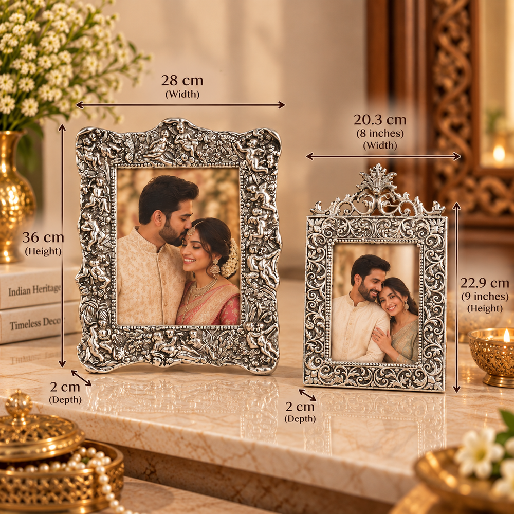 Two ornate silver picture frames with decorative scrollwork, shown on a marble surface with overlaid dimension arrows and text indicating width, height, and depth. The background is a warm indoor setting with decorative gold-toned objects and flowers.