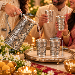 An ornate silver-toned metal teapot with intricate floral engravings is shown pouring liquid into two matching engraved metal cups on a decorative tray, with people holding additional cups in the background. Measurement arrows and labels indicate the teapot's dimensions (22 cm, 13 cm, 9 cm, 7 cm, 10 cm).