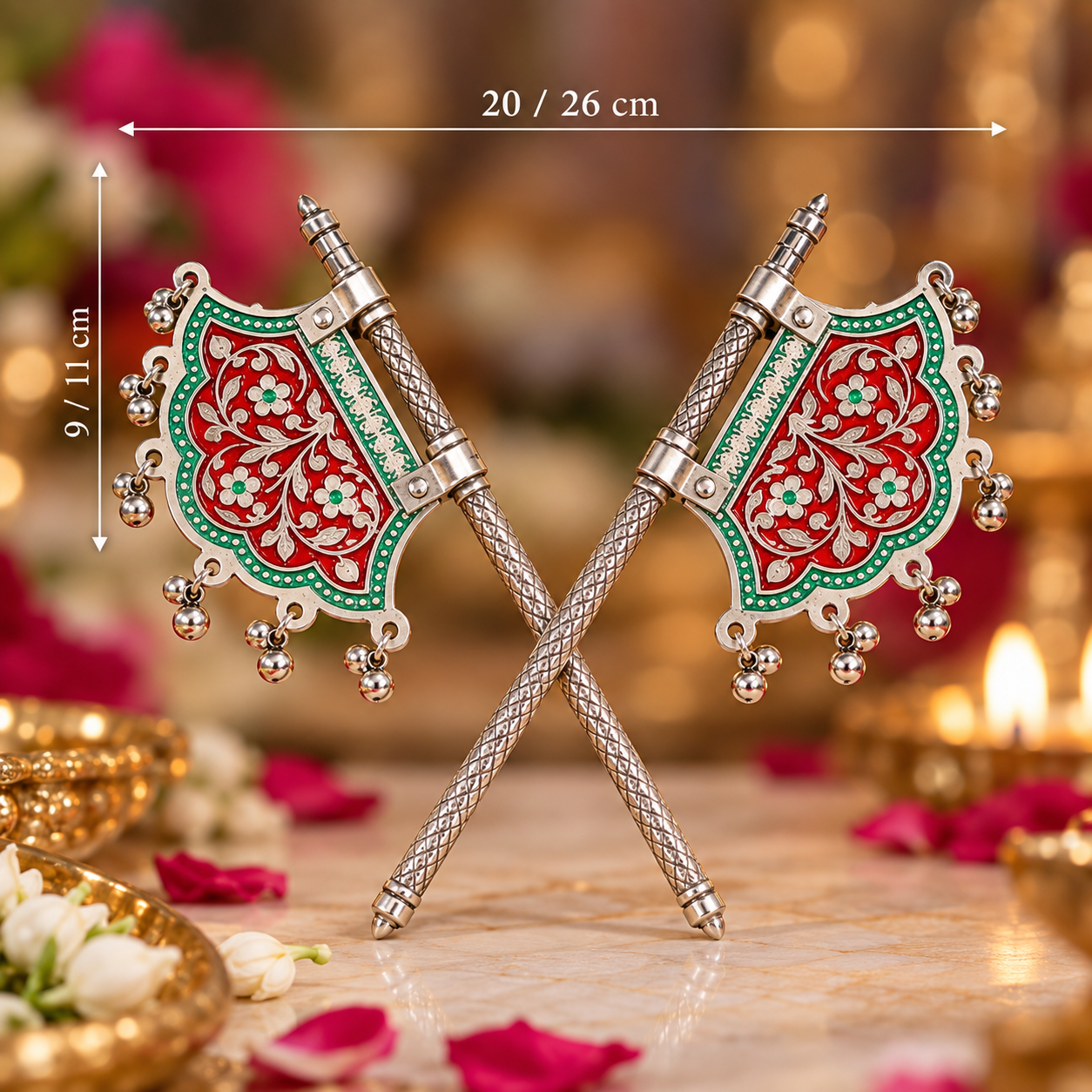 Two ornate decorative axe-shaped ornaments with red, green, and silver floral engravings, crossed over each other on a marble surface with warm blurred background lights and flowers.