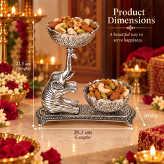 Silver-toned elephant-shaped serving tray filled with nuts and fruits, shown on a decorated table with candles and flowers. White dimension lines and text indicate product measurements: 21.