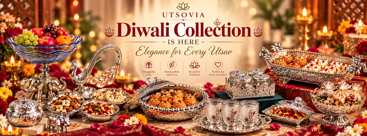 A festive Diwali table display with ornate silver serving dishes, bowls of sweets and fruit, and the text 'UTSOVIA Diwali Collection IS HERE Elegance for Every Utusu' centered on a warm decorated background.