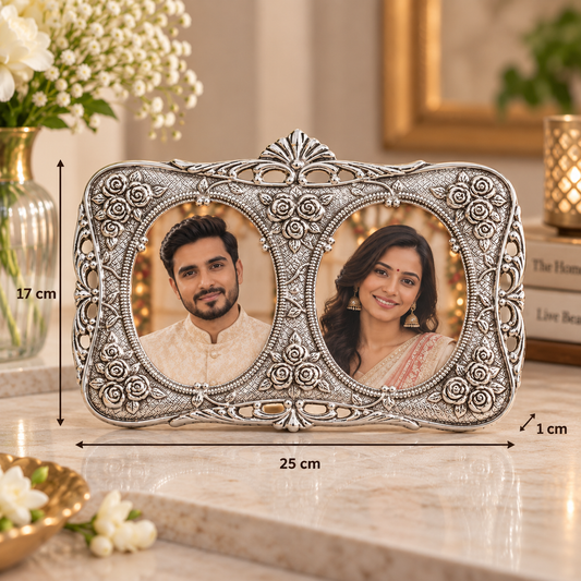 An ornate silver double-photo frame with detailed floral carvings, shown on a marble countertop with dimension lines indicating 25 cm width, 17 cm height, and 1 cm depth. The photos inside the frame show a man and a woman.