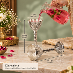 An ornate silver-toned glass goblet with engraved detailing, shown on a marble surface with overlaid dimension labels indicating 18 cm length, 25 cm height, and 8 cm top diameter. A hand pours pink liquid from a glass pitcher into one goblet, and a text box at the bottom reads Dimensions.