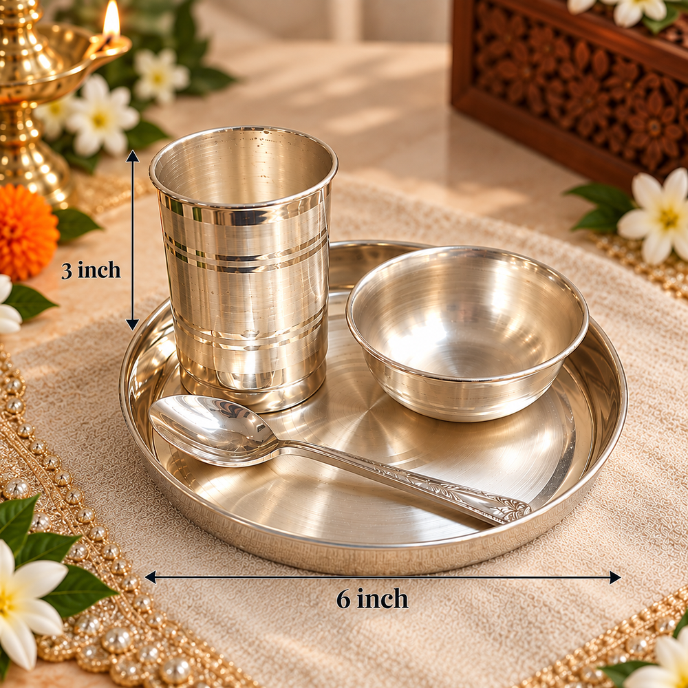 A stainless steel Indian-style prayer tray set with a cup, bowl, and spoon on a round tray, shown with dimension labels indicating 6 inch width and 3 inch height. The tray is placed on a beige fabric with decorative flowers and a brass oil lamp in the background.