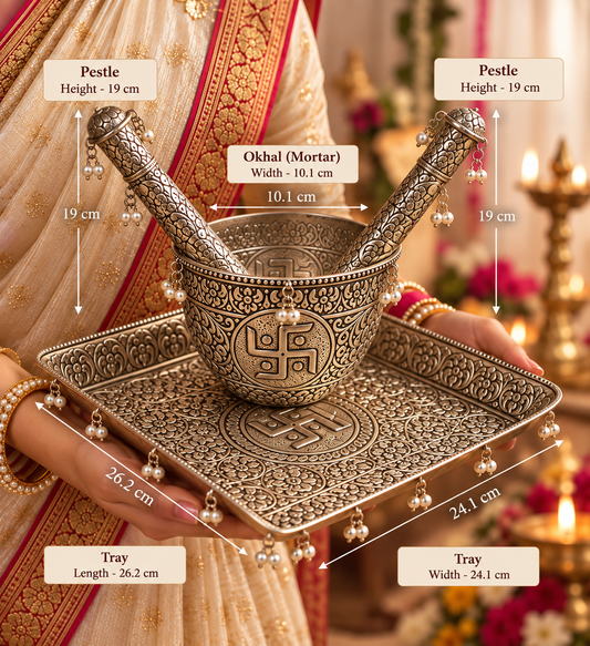 An ornate silver-toned Indian brass/metallic kitchen set including a pestle, mortar, and decorative tray, shown with overlaid dimension labels and arrows. A person in traditional clothing is partially visible holding the set, and a warm lit indoor background with candles appears behind it.