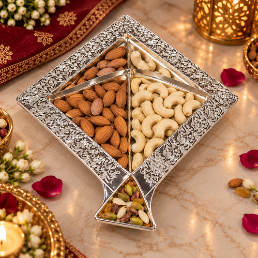 A decorative silver-toned four-compartment nut and almond tray filled with almonds, cashews, and mixed nuts, styled on a marble surface with warm lighting and floral accents.