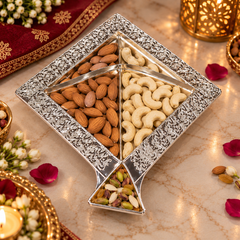 A decorative silver-toned four-compartment nut and almond tray filled with almonds, cashews, and mixed nuts, styled on a marble surface with warm lighting and floral accents.
