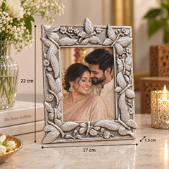 An ornate silver-toned picture frame with embossed floral and leaf designs, shown standing on a marble surface with printed dimensions overlaid (17 cm width, 22 cm height, and 1.5 cm depth).