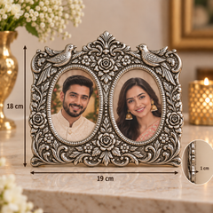 An ornate silver-toned double oval photo frame with floral and bird details, shown on a marble surface with overlaid dimension markers indicating 18 cm height, 19 cm width, and a 1 cm inset detail. Two sample portrait photos are inserted into the oval openings.