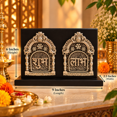 A black rectangular decorative plaque or box with two ornate silver arch motifs and Devanagari text, shown on a tabletop with dimension callouts reading 9 inches length, 6 inches height, and 2.5 inches width.