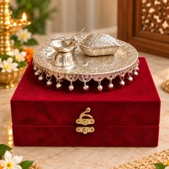 A silver-toned decorative tray set with a small lamp and a carved box, displayed on top of a deep red velvet box with a gold clasp in a warm indoor setting.