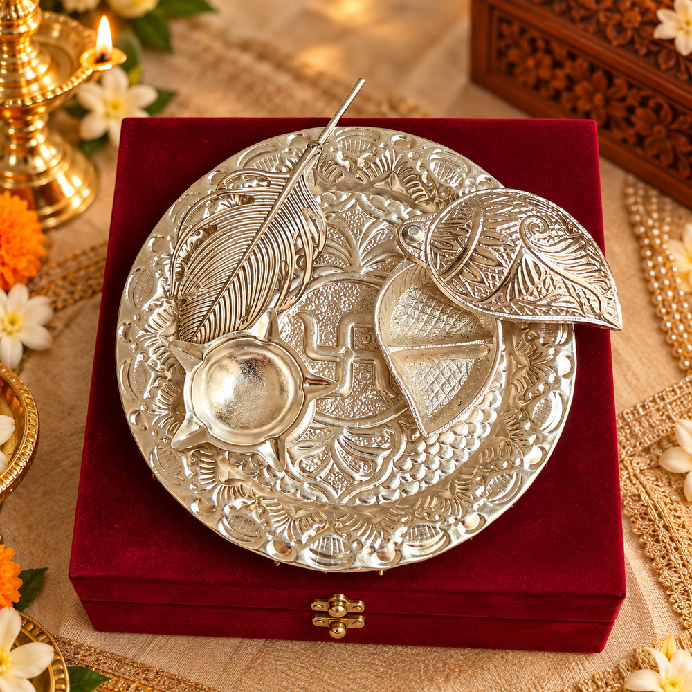 An ornate silver-toned plate with embossed floral patterns and a swastika symbol, displayed on a deep red velvet box. The plate includes a small bowl and two leaf-shaped pieces, set against a decorated festive background with flowers and candles.