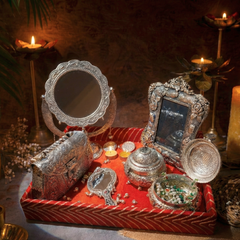 Decorative silver vanity set on a red tray with candles and plants in the background