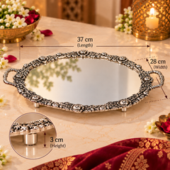 An ornate silver oval tray with a mirror center, decorative filigree border, and small feet, shown on a beige marble surface with overlaid dimension labels for length, width, and height. A circular inset highlights the 3 cm height detail.
