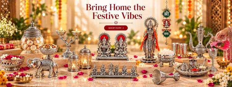 A festive Diwali-themed product display featuring an array of ornate silver-colored decorative items, including a large Lord Rama statue, a silver elephant figurine, brass oil lamps, and ceremonial vessels, arranged on a marble table with rose petals and warm golden background lights. Text at the top reads 'Bring Home the Festive Vibes' with a 'SHOP NOW' button.