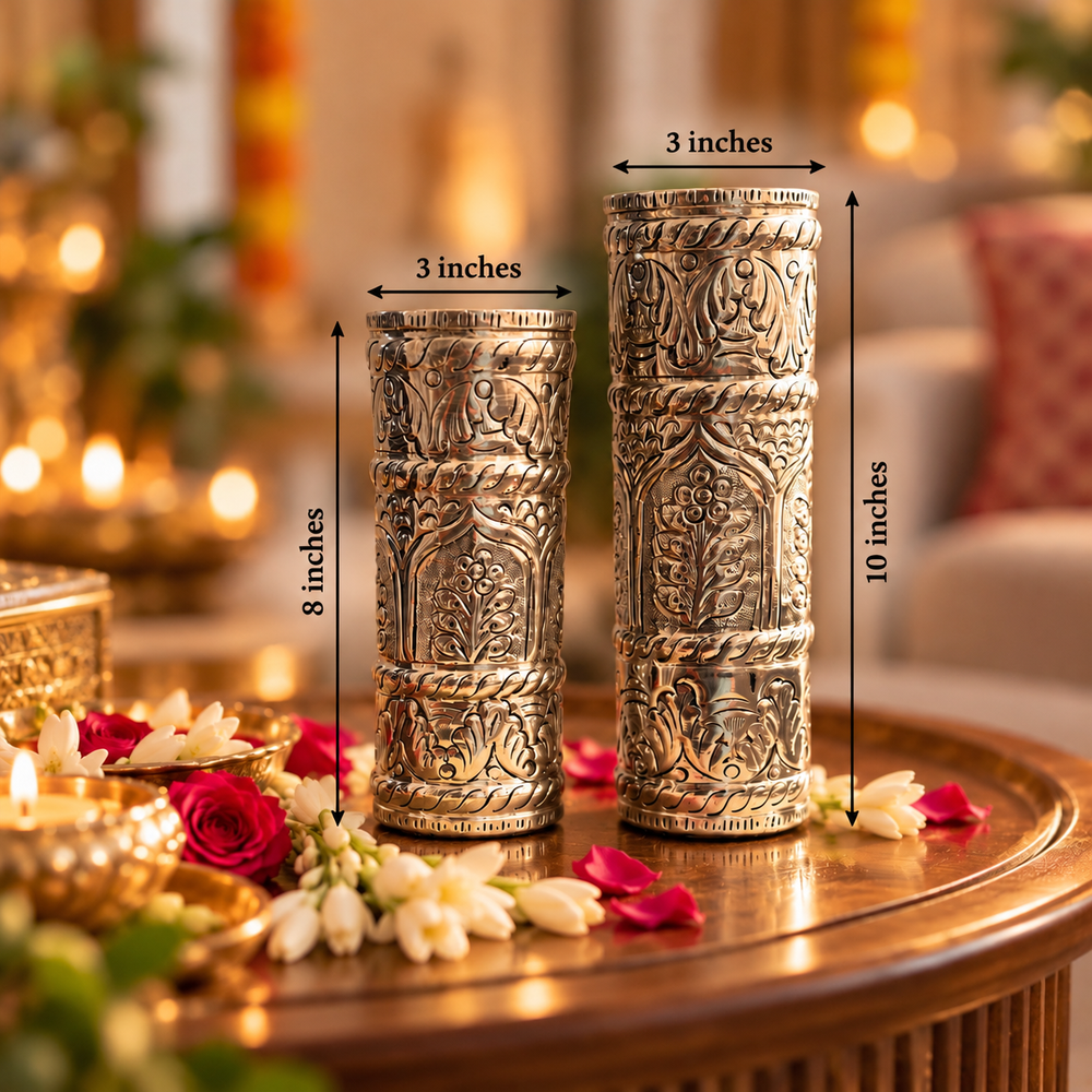 Two ornate silver-toned decorative candle holders with intricate carvings, shown on a wooden table in a warmly lit living room. Black measurement arrows and text labels indicate the dimensions: both are 3 inches wide, one is 8 inches tall, and the other is 10 inches tall.