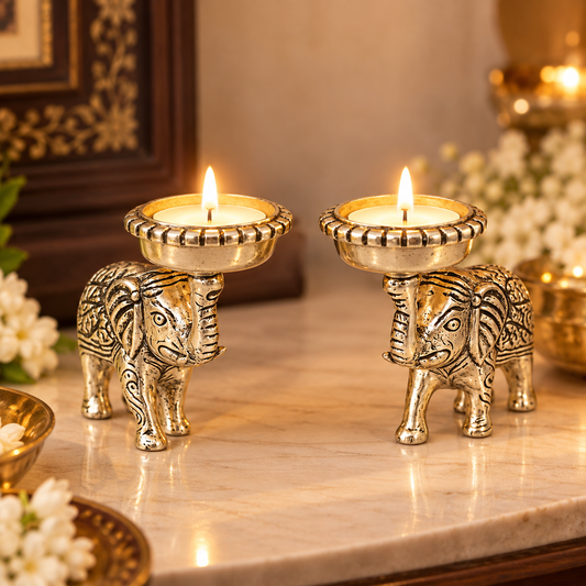 Two ornate elephant-shaped brass candle holders with lit tealight candles, displayed on a polished marble surface with warm, decorative background elements.