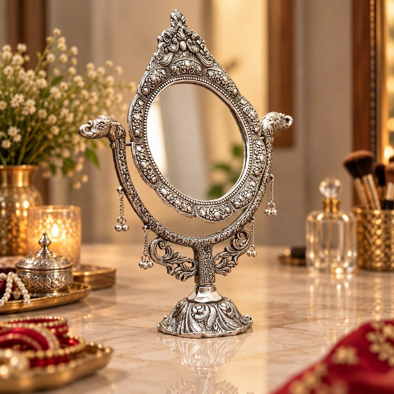 An ornate silver vanity mirror with intricate carvings and hanging charms, displayed on a marble tabletop in a warm, decorated room.