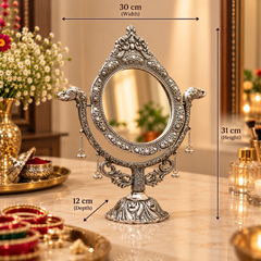 An ornate silver vanity mirror with decorative animal-head supports and hanging bells, shown on a marble tabletop in a styled bathroom setting. Measurement arrows and labels indicate the mirror's dimensions: 30 cm width, 31 cm height, and 12 cm depth.