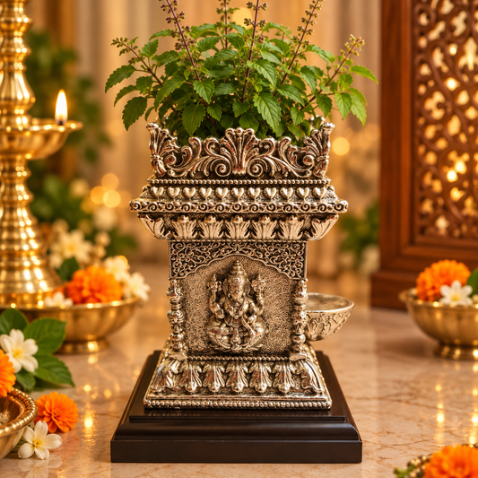 An ornate silver-toned Ganesha idol planter with a green leafy plant, displayed on a dark wooden base on a marble surface with warm bokeh background.