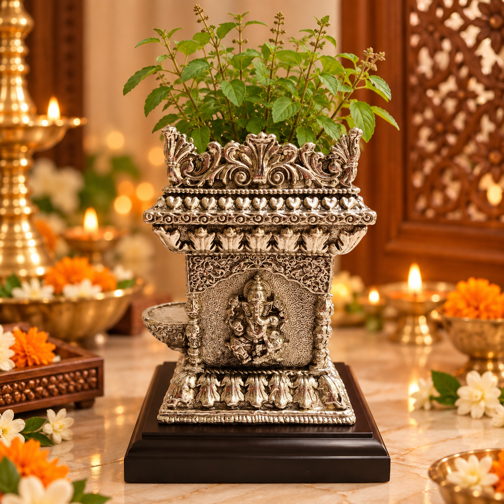 An ornate silver-toned decorative planter shaped like a miniature temple, filled with green leafy stems, displayed on a dark wooden base on a marble surface with warm ambient lights and floral decor in the background.