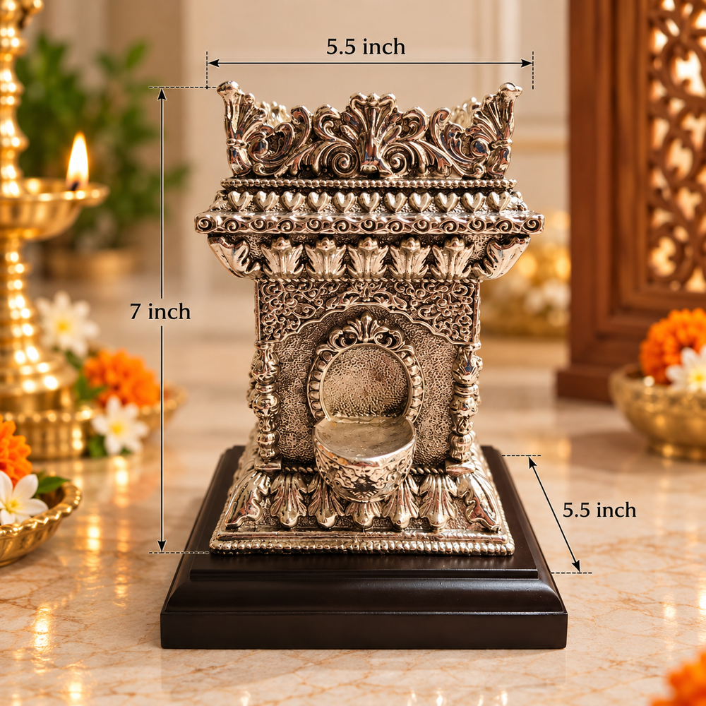 An ornate silver-toned miniature diya holder with a black base, shown on a marble-like surface with dimension labels indicating 7 inch height and 5.5 inch width/depth.