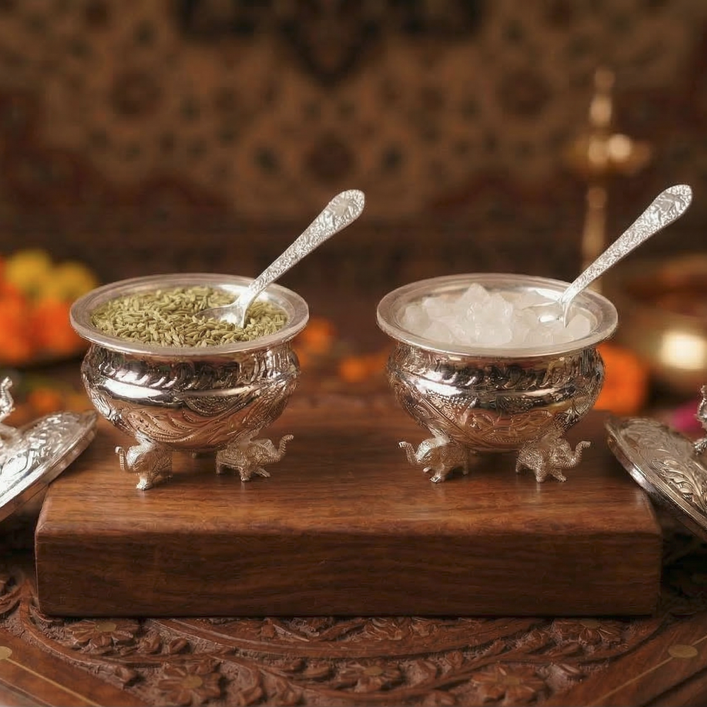 Two silver bowls with spoons on a wooden surface with a blurred background
