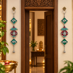 Two decorative hanging wall ornaments with metallic rings, green diamond-shaped panels with white Devanagari text, and colorful floral motifs are displayed on either side of a carved wooden doorway in a warmly lit interior.